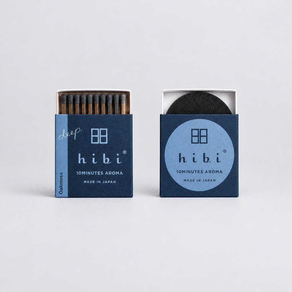 Two hibi 10minutes Aroma matchboxes on a clean white background, one showing the dark matchsticks inside and the other showing the black circular insert.