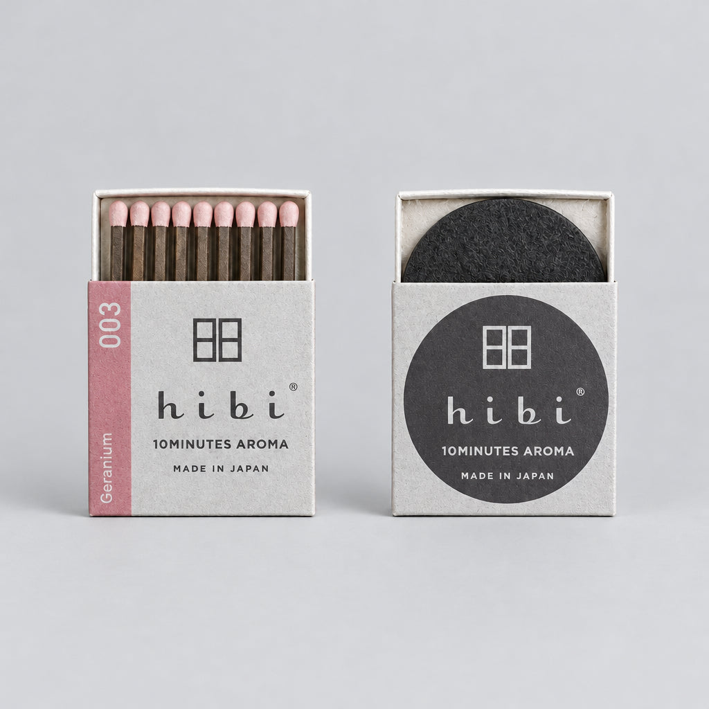 Two Hibi 10minutes Aroma matches on a rustic wooden background. The left matchbox is open, showing light wood matches with dark tips, and the right matchbox is closed, showing a round black charcoal filter.